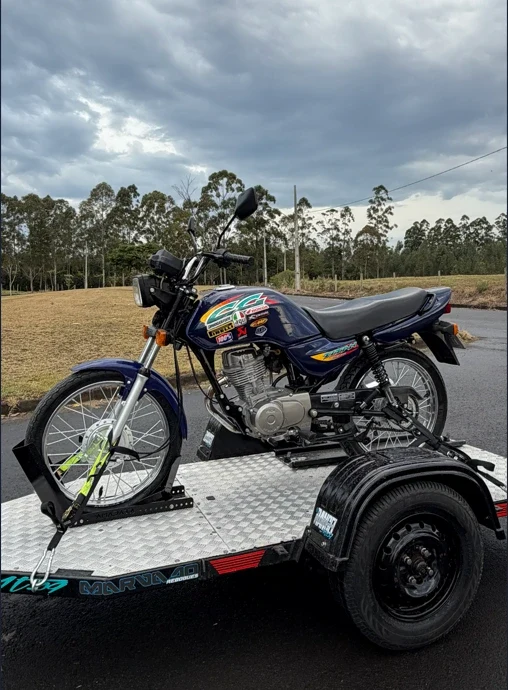 Lado oposto da Titan azul, com adesivos, motor, banco e roda dianteira visíveis