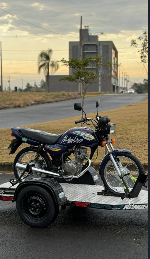 Titan azul completa, vista de lado sobre a carretinha, em rua com céu de fim de tarde
